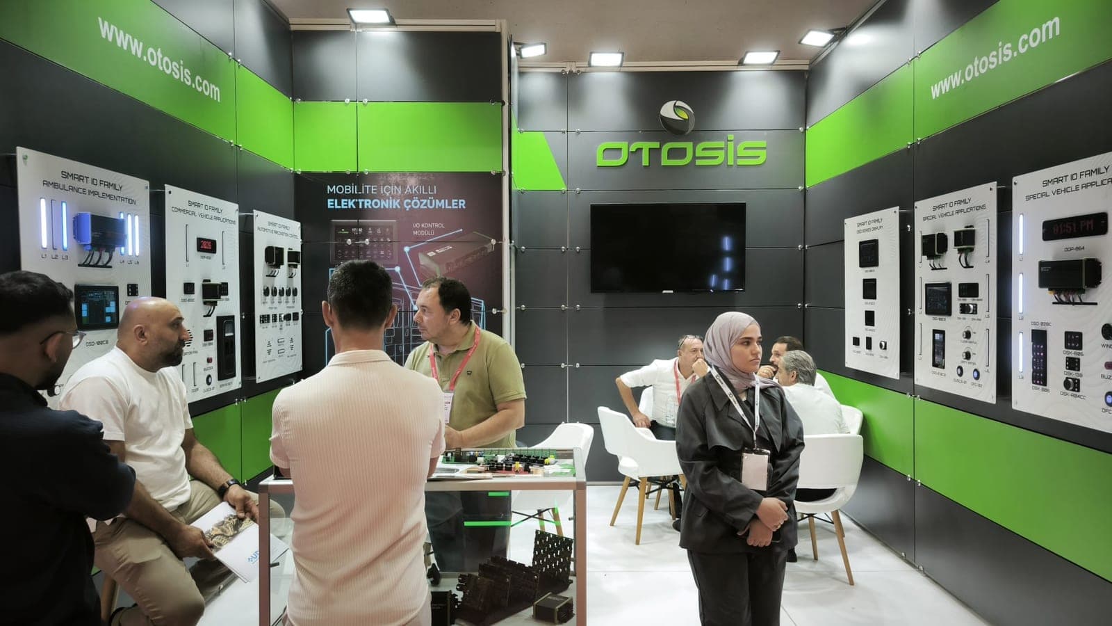 Otosis fuar standının genel görünümü: duvarlarda ürün panoları, ziyaretçiler